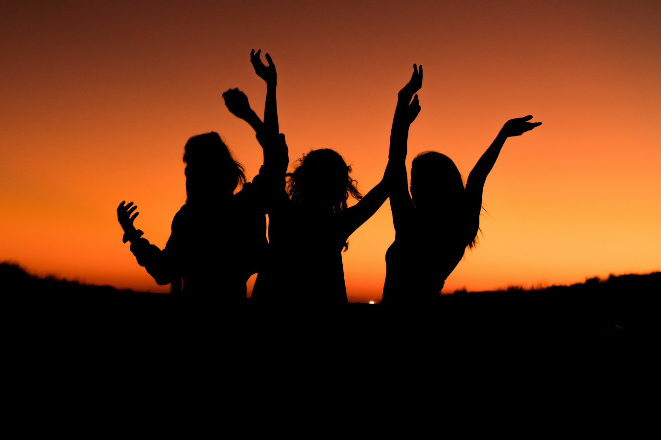 Shadows of three women celebrate at sunset.