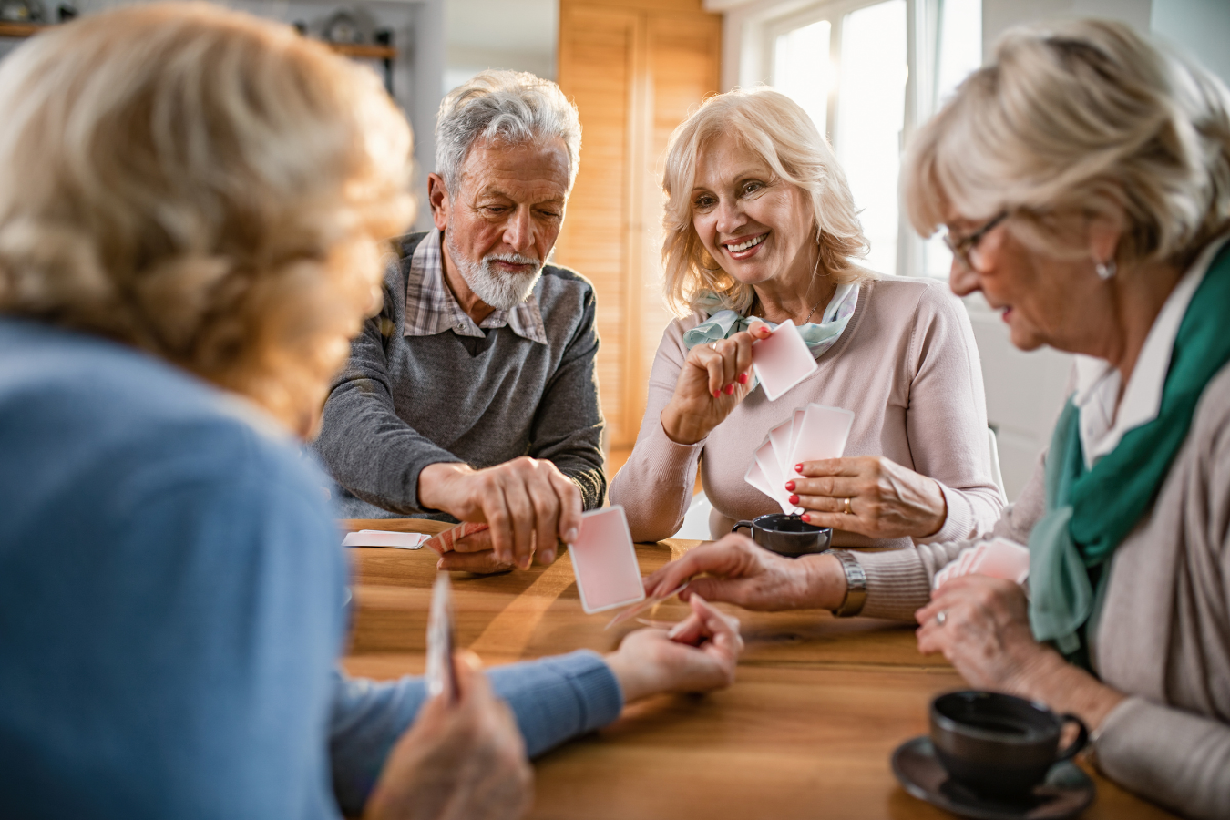 Four friends sit around at table laughing and playing cards.