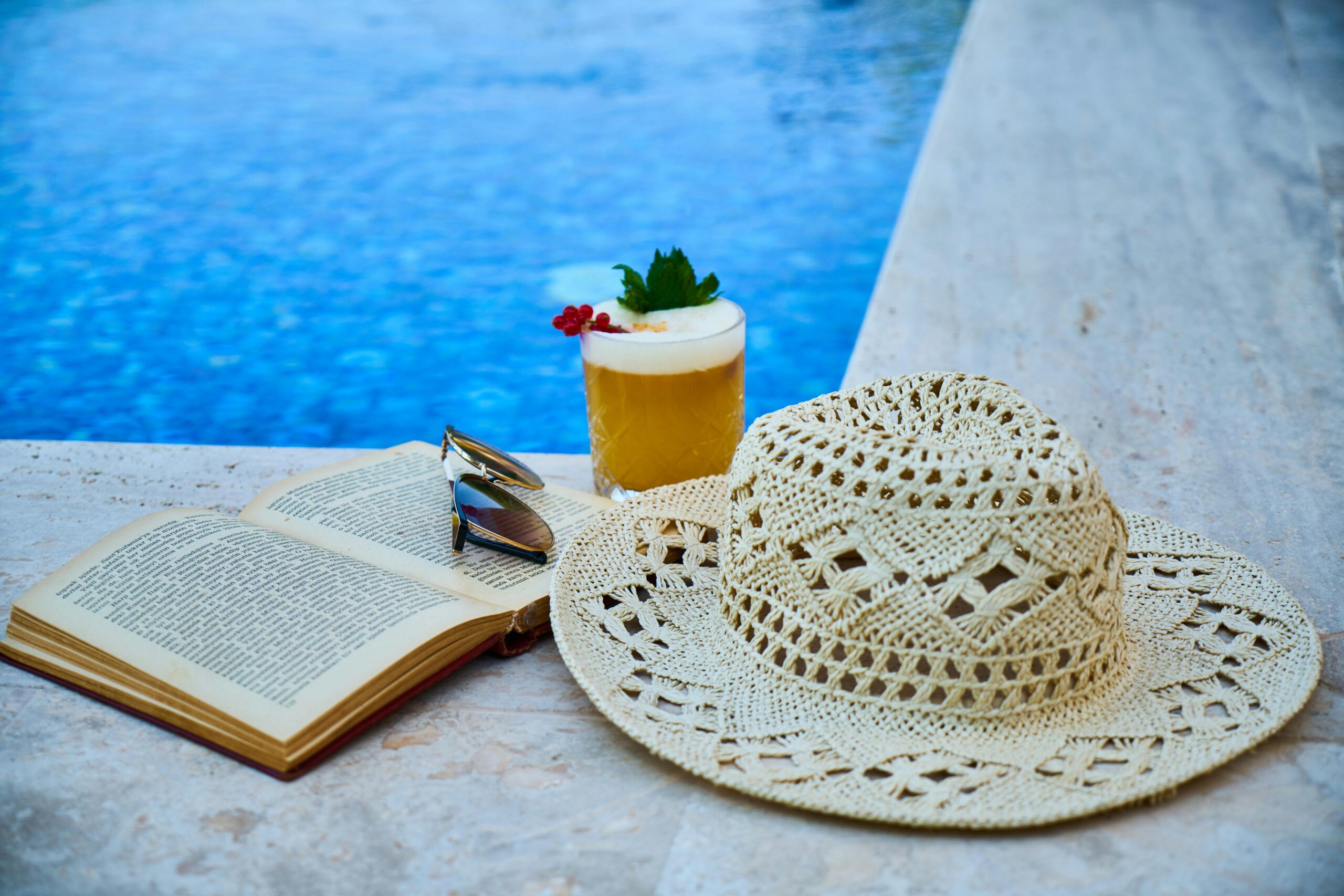 Sunhat, cocktail, and book at pool's edge.